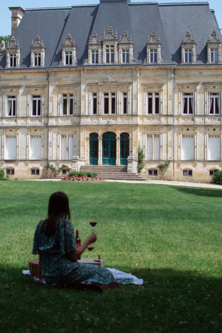 Femme assise dans l'herbe dégustant du vin devant le Château Lestage
