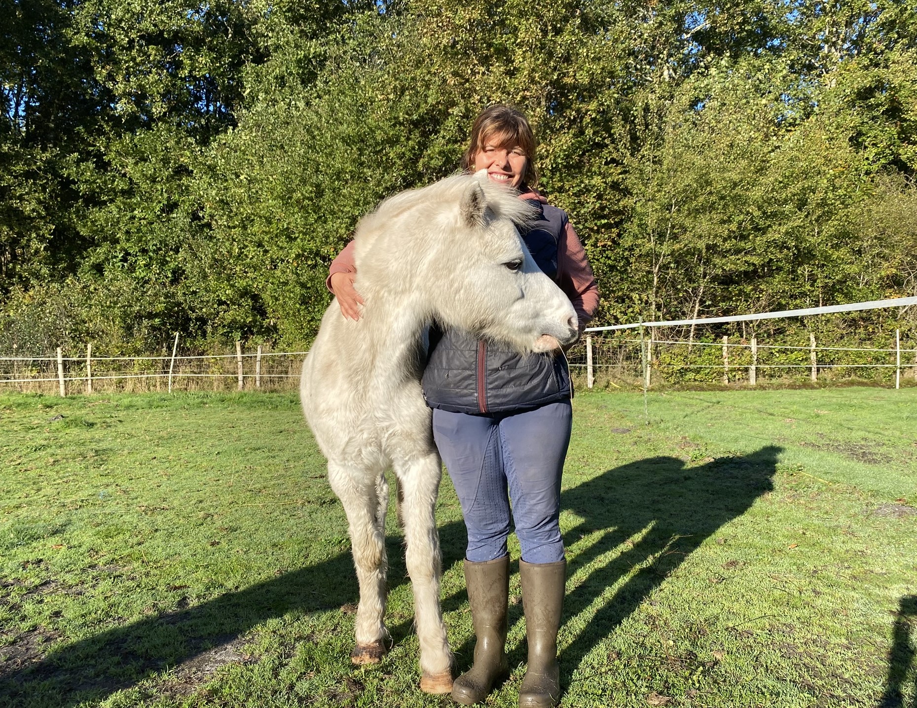 un petit poney shetland blanc et sa propriétaire de face se faisant un calin