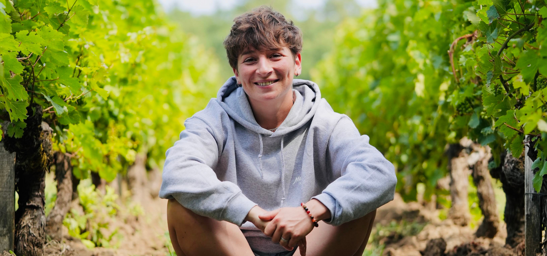 lucie mancais vigneronne, de face, assise dans un rang de vigne souriant