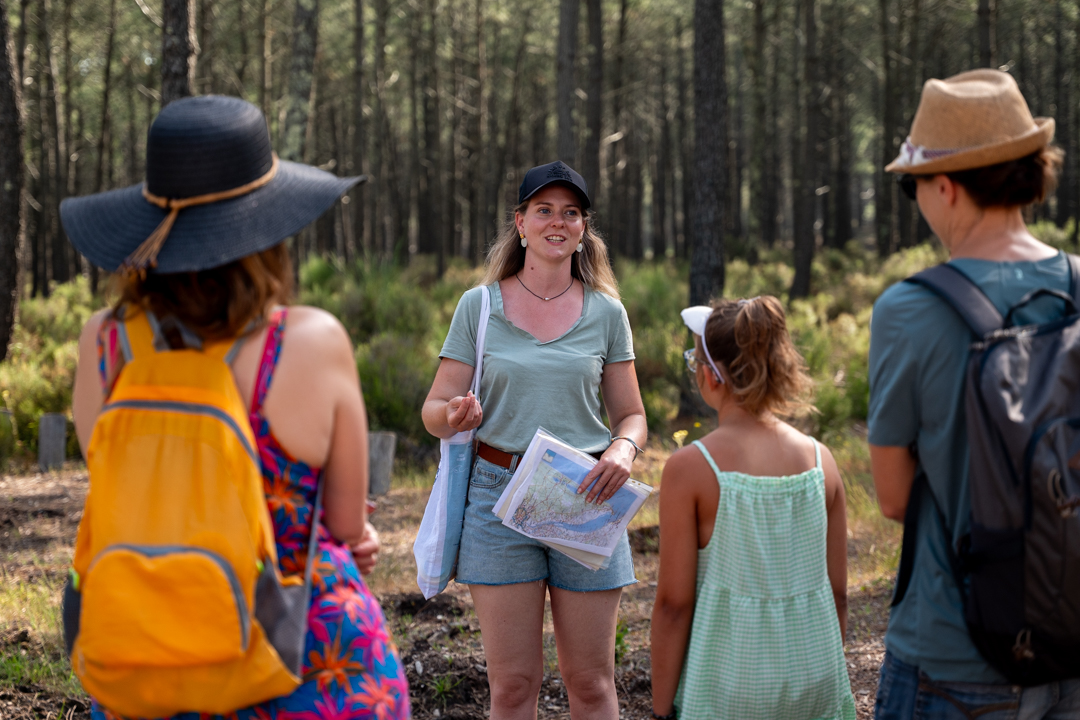 une guide naturaliste de face en arrière plain et des touristes de dos écoutant ses explications au premier plan